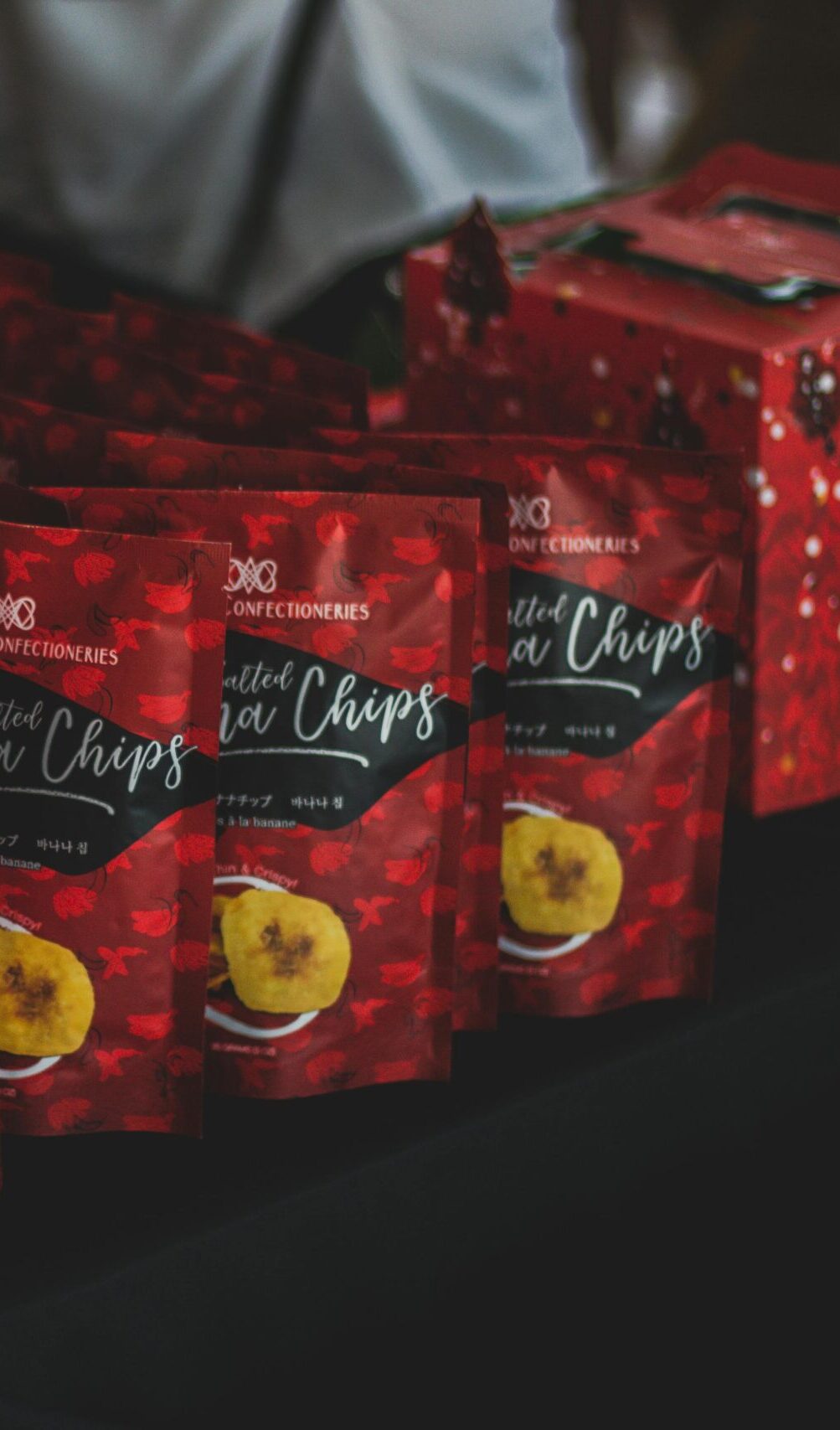 Packaged banana chips displayed with a promotional 'Buy 4 Take 1' sign at an indoor sale event.